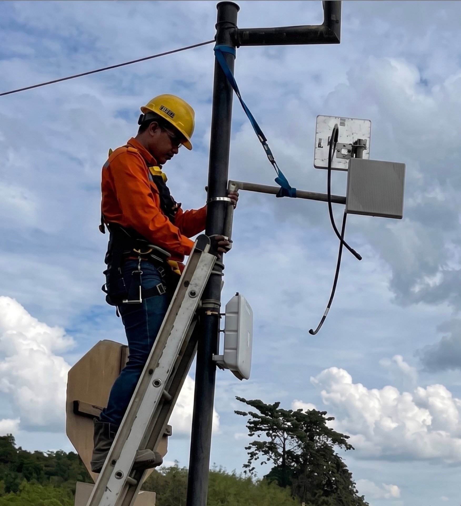 A technician on a ladder installing wireless equipment on a pole at a remote site.